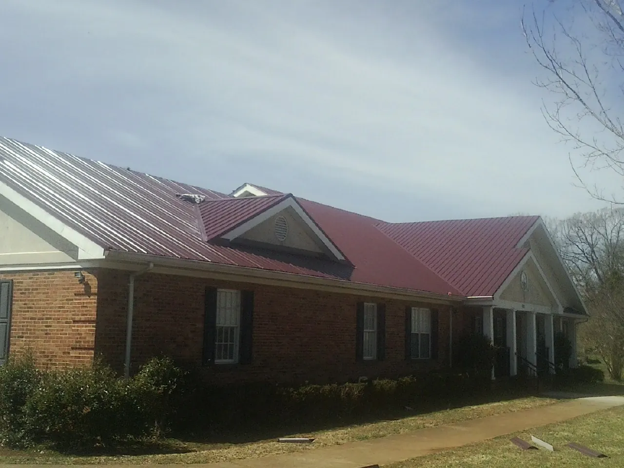 Red metal roof with gabled entries on a long brick building, from a Hail Damage Roof Repair job in Erving