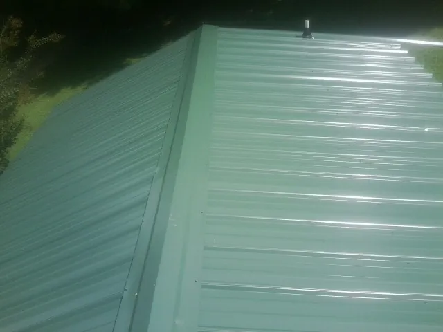New green metal panels meeting at the ridge of a roof — Flat Roof Repair work by our crew in Erving