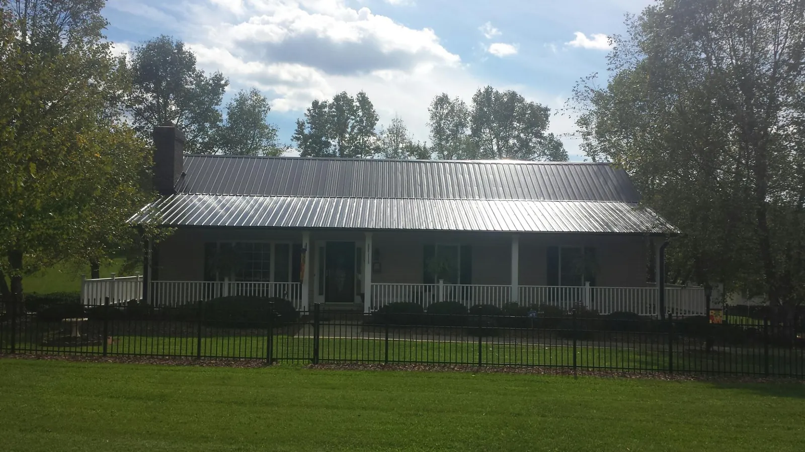 Gray metal roof on a brick ranch with a full width front porch — Gutter Guard Installation work by our crew in Erving