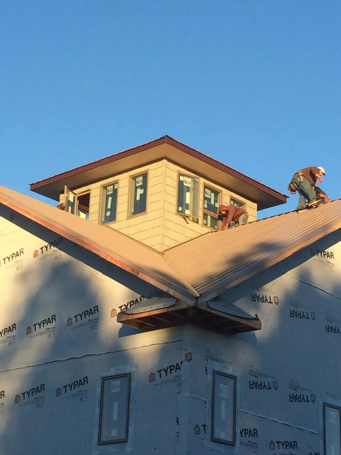Roofers working around a rooftop cupola on a new metal roof at sunset — Roof Waterproofing in Erving by Roofing Brothers